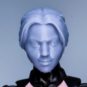 May include: A light blue figurine head with detailed hair and facial features. The figure is wearing a black outfit with a pink chest piece and a yellow and red accent. The figure is a collectible item.