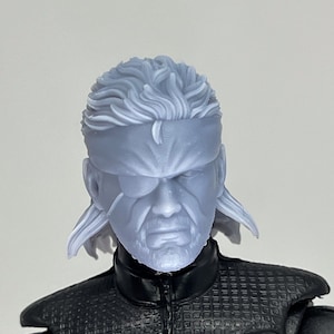 May include: A grey plastic action figure head with a grey eyepatch and a long grey ponytail. The head is sculpted with a detailed face and hair.