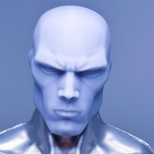 May include: A close-up of a futuristic action figure with a silver metallic torso and a pale blue head. The figure has a stern expression and is set against a solid blue background. The figure's design suggests a science fiction or superhero theme.