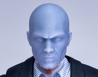 May include: A blue-faced action figure wearing a black suit, white shirt, and blue patterned tie. The figure has a serious expression.