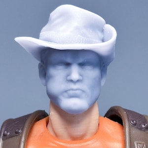 Op de afbeelding: Een close-up van het hoofd en de torso van een speelgoedactiefiguur. De figuur heeft een lichtblauwe cowboyhoed en gezicht. De figuur draagt een oranje shirt met een tijgerafbeelding en bruine bandjes.