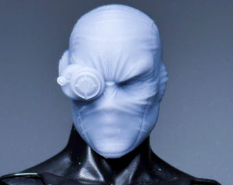 May include: A black action figure with a light blue head and face covering. The figure has a detailed, muscular physique and a mask-like face with a single, circular eyepiece. The figure is a collectible item.