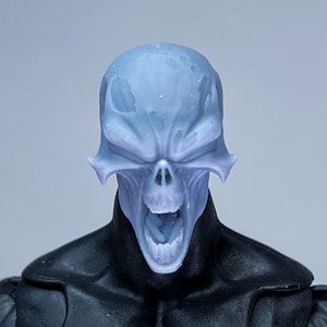 Può includere: Primo piano della testa di una action figure blu e bianca con un viso a forma di teschio e la bocca aperta. La figura indossa un abito bianco e nero.