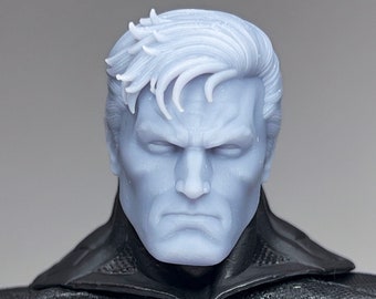 May include: A close-up of a Batman action figure's head, featuring a detailed sculpt of the character's face and hair. The figure's head is painted in a light blue color, giving it a realistic appearance.