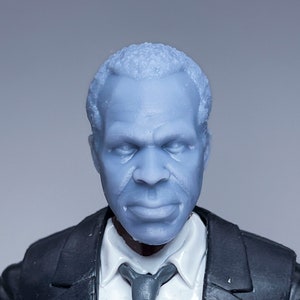 Könnte beinhalten: Ein grauer Plastik-Actionfigur-Kopf mit kurzen Haaren, der einen schwarzen Anzug und eine graue Krawatte trägt. Die Figur hat einen ernsten Gesichtsausdruck.