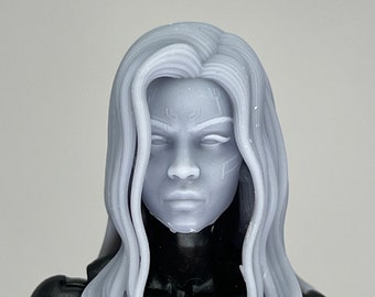 May include: A close-up of a gray plastic action figure head with long, wavy hair. The figure has a detailed face with a serious expression.