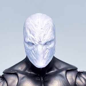 Könnte beinhalten: Ein weißer Plastik-Actionfigur-Kopf mit einer detaillierten, strukturierten Maske. Die Maske hat einen bedrohlichen Ausdruck mit einem breiten Mund und scharfen Zähnen.