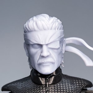 May include: A white plastic action figure head with a black eye patch and a white headband. The figure has a sculpted face with a moustache and a serious expression.