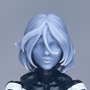 Puede incluir: Primer plano de una figura de acción femenina con el pelo corto y blanco. Lleva un traje negro y blanco con una pieza de pecho blanca. La figura tiene una cara pintada realista.