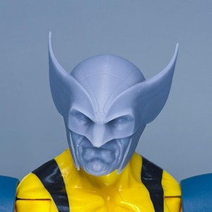 May include: A close-up of a blue and yellow action figure with a grey plastic head and ears. The figure is wearing a yellow and black costume.