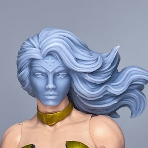 Puede incluir: Primer plano de una figura de acción femenina con el pelo largo y plateado que fluye. Lleva un traje negro y dorado con una estrella en la frente.