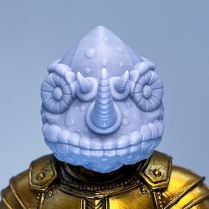 Puede incluir: Un casco gris de camaleón impreso en 3D con una superficie texturizada y un cuerno grande y puntiagudo en la parte superior. El casco tiene dos ojos grandes y redondos a los lados.