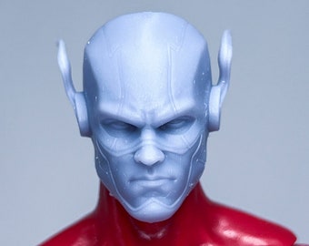 May include: A close-up of a blue action figure head with red and yellow details. The figure has a serious expression and is wearing a red suit.