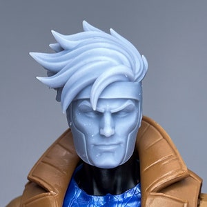 以下が含まれることがあります： 白いとげとげの髪型と茶色と青のジャケットを着たプラスチック製アクションフィギュアの頭部のクローズアップ。フィギュアは真剣な表情で、青とピンクの胸部パーツを付けている。