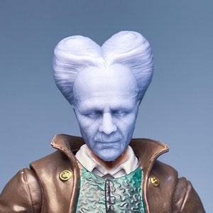 May include: A close-up of a plastic action figure head with a sculpted hairstyle. The figure has a pale complexion and is wearing a brown leather jacket with gold buttons.