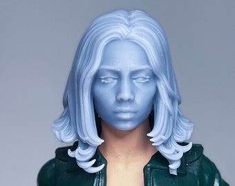 Puede incluir: Cabeza de figura azul claro con los ojos cerrados y cabello ondulado. La figura lleva una chaqueta verde oscuro con botones dorados sobre una blusa negra. El fondo es gris claro liso.
