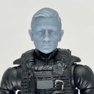 May include: A gray plastic action figure head with short, styled hair. The head is attached to a black action figure body wearing a tactical vest with pouches and straps.