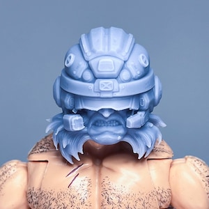 Può includere: Una testa di action figure stampata in 3D di colore grigio con un casco dettagliato e una barba. Il casco ha una visiera e diversi pulsanti e dettagli. La figura ha un'espressione feroce.