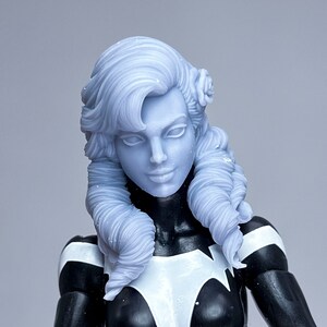 May include: A black and white action figure with a white sculpted head and long, wavy, white hair. The figure is wearing a black and white costume with a white stripe down the center.