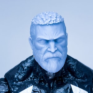 May include: Close-up of a blue and black action figure head with a white symbol on the chest. The figure has a white beard and a serious expression.