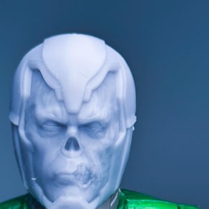 May include: A white plastic action figure head with a green and black body. The head has a skull-like design with a detailed face.