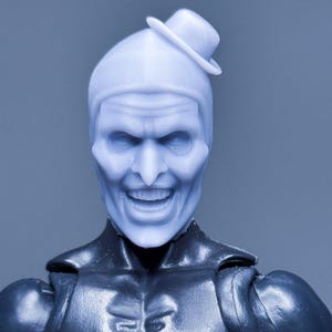 Könnte beinhalten: Hellblauer Actionfigurenkopf mit einem lächelnden Gesicht und einem kleinen Hut. Die Figur hat ein detailliertes, ausdrucksstarkes Gesicht und ist an einem schwarzen Torso befestigt. Die Gesamtästhetik erinnert an ein Vintage-Spielzeug.