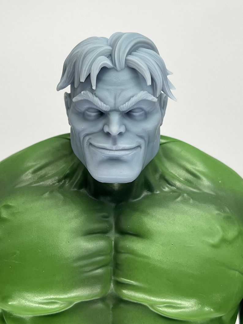 May include: A close-up of a gray, sculpted head of a man with short, gray hair. The head is attached to a green, sculpted body. The man has a serious expression on his face.