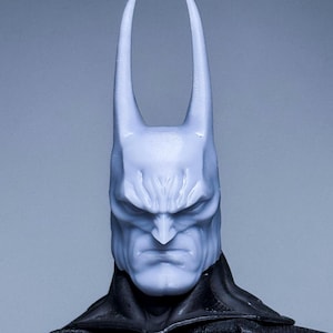Puede incluir: Primer plano de la cabeza de una figura de acción de Batman con una cara esculpida detallada y orejas puntiagudas. La cabeza está pintada de color azul claro.