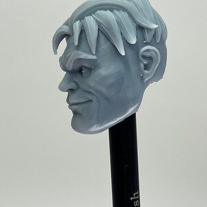 May include: A 3D printed gray plastic head sculpt of a man with short, styled hair. The head is angled to the side, and the man has a slight smile on his face.