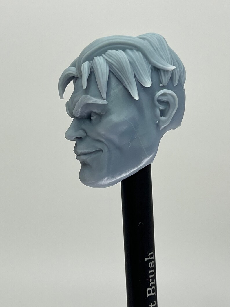 May include: A 3D printed gray plastic head sculpt of a man with short, styled hair. The head is angled to the side, and the man has a slight smile on his face.