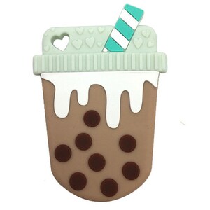 May include: A bubble tea-shaped baby teether in light brown, white, and teal. The teether features a mint green lid with heart cutouts and a teal and white striped straw. Dark brown circles represent the boba pearls.