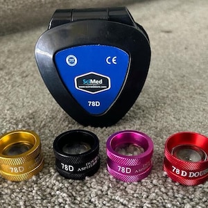 May include: A set of six 7.8D double aspheric ophthalmic lenses in various colors, including blue, gold, black, pink, red, and green. The lenses are arranged in a row on a gray carpet. A black case with a blue label that reads "SciMed" and "7.8D" is also included.