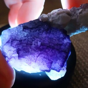 May include: A large, purple fluorite crystal with a rough, textured surface. The crystal is illuminated from below, highlighting its intricate details.