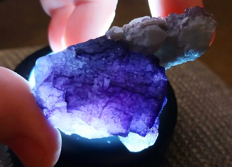 May include: A large, purple fluorite crystal with a rough, textured surface. The crystal is illuminated from below, highlighting its intricate details.