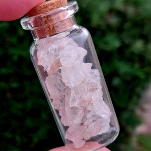 May include: A small glass bottle with a cork stopper filled with clear, pink, and white crystal chunks.