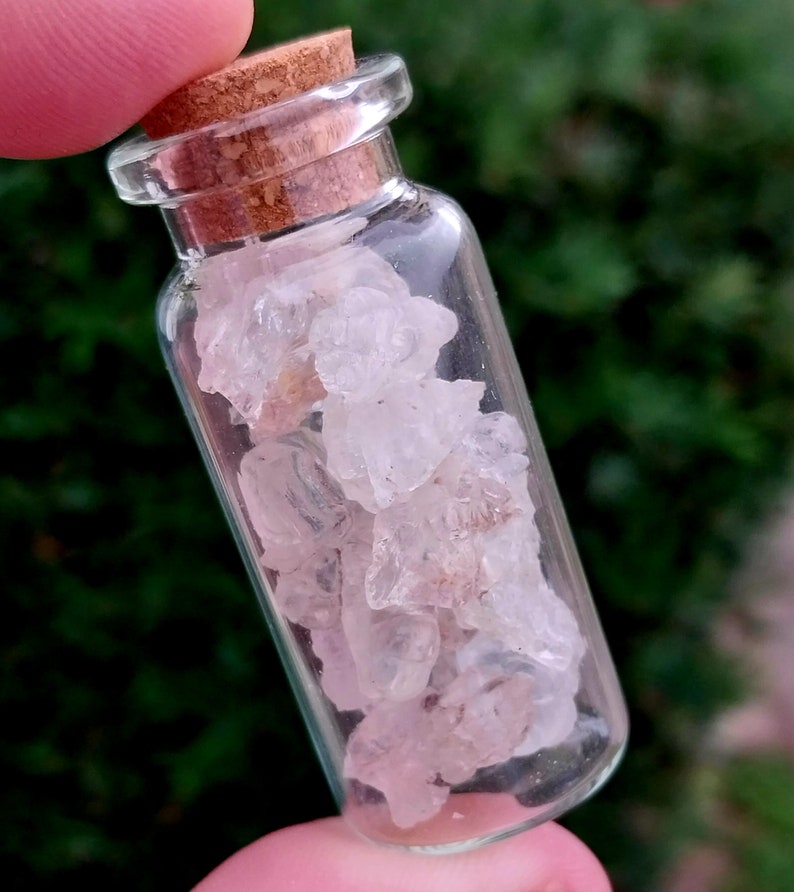 May include: A small glass bottle with a cork stopper filled with clear, pink, and white crystal chunks.