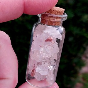 May include: A small glass bottle with a cork stopper filled with clear and pink crystals.