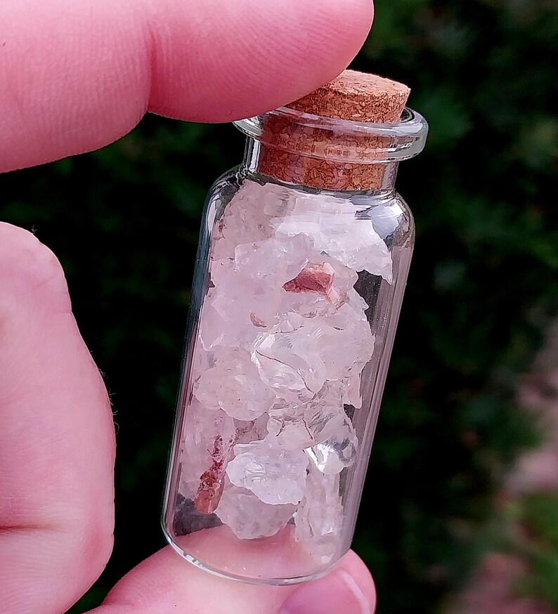 May include: A small glass bottle with a cork stopper filled with clear and pink crystals.