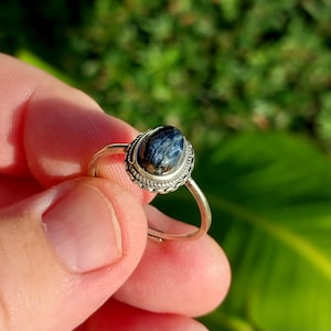 May include: A silver ring with a blue and black tiger's eye gemstone set in a silver bezel.