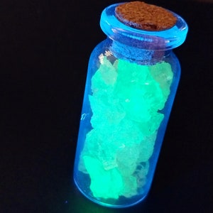 May include: A small glass bottle with a cork stopper filled with glowing green crystals.