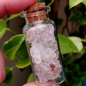 May include: A small glass bottle with a cork stopper filled with clear quartz crystals and a few small pink crystals.