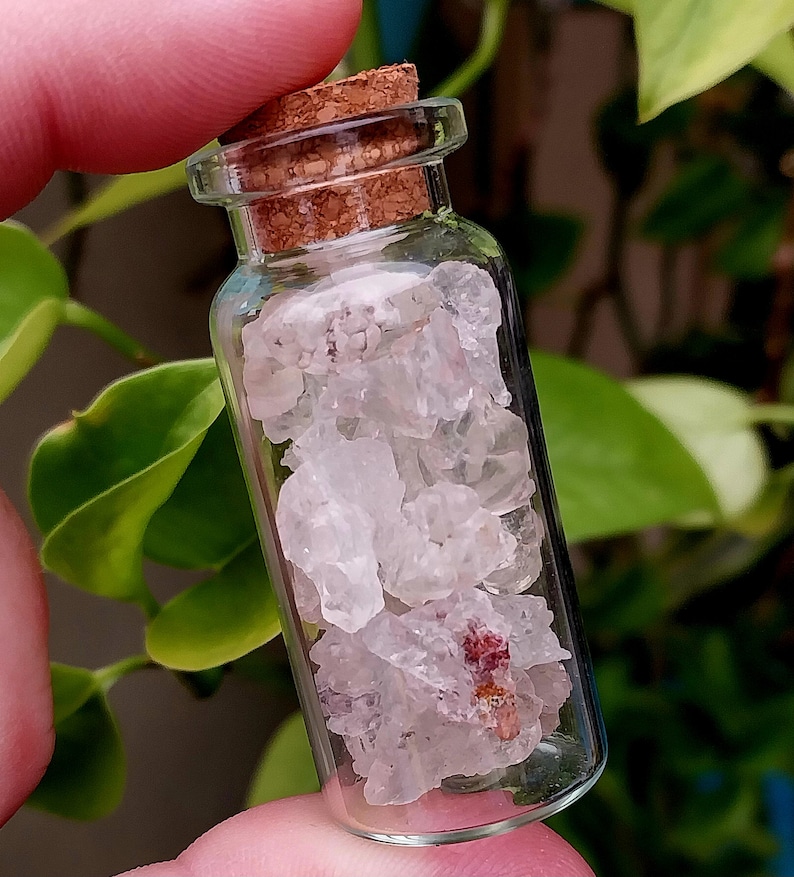 May include: A small glass bottle with a cork stopper filled with clear quartz crystals and a few small pink crystals.