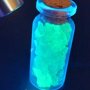 May include: A glass bottle with a cork stopper filled with glowing green crystals. The bottle is clear and the crystals are a bright, vibrant green.