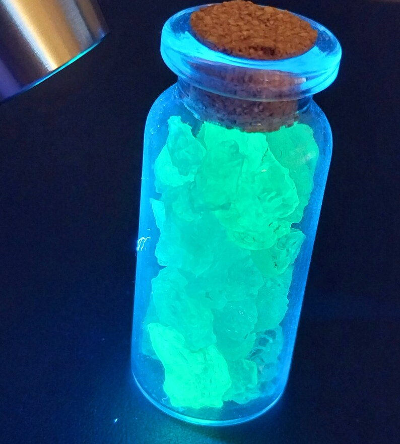 May include: A glass bottle with a cork stopper filled with glowing green crystals. The bottle is clear and the crystals are a bright, vibrant green.
