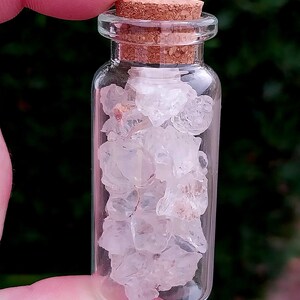 May include: A small glass bottle with a cork stopper filled with clear, white crystals. The bottle is held in a hand.
