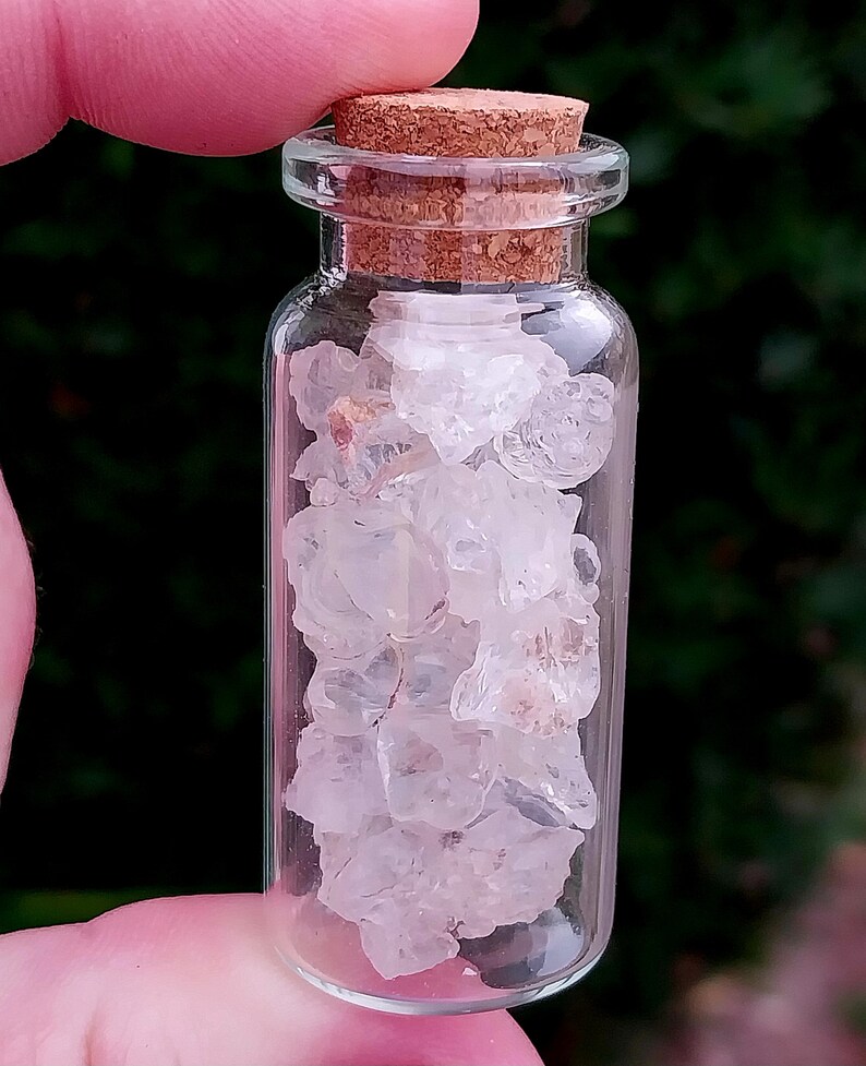 May include: A small glass bottle with a cork stopper filled with clear, white crystals. The bottle is held in a hand.