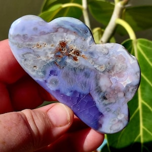 May include: A purple and white agate heart-shaped stone with brown inclusions. The stone is polished and has a smooth surface.