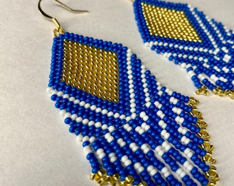 Op de afbeelding: Een paar blauwe en gouden kralen oorbellen met een diamantvorm aan de bovenkant en een franje van kralen die naar beneden hangen.