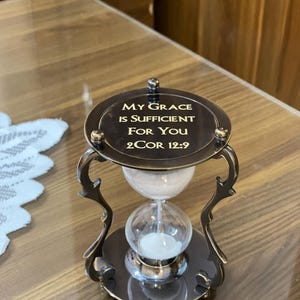 Könnte beinhalten: Eine Sanduhr aus Messing mit der Inschrift "My Grace is Sufficient for You 2 Cor 12:9".