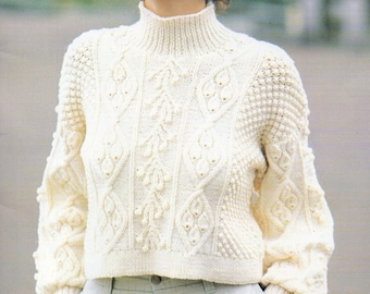May include: A white knitted sweater with a high neck and a cable knit pattern. The sweater has a cropped length and long sleeves with a puffed detail at the shoulders.